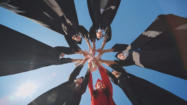 College graduates join hands with diplomas standing in a circle