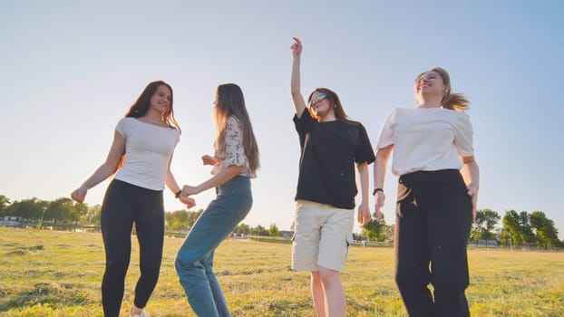 Funny jolly friends dancing in the city meadow in the evening