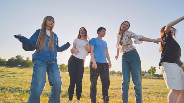 Funny jolly friends dancing in the city meadow in the evening