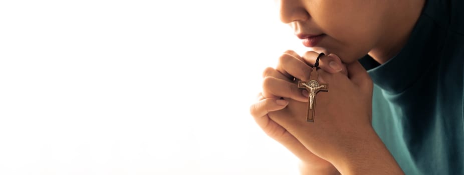 Praying female hand holding cross while praying to god faithfully. Concept of hope, religion, faith, christianity and god blessing for happiness. Bright light, white blurring background. Burgeoning.