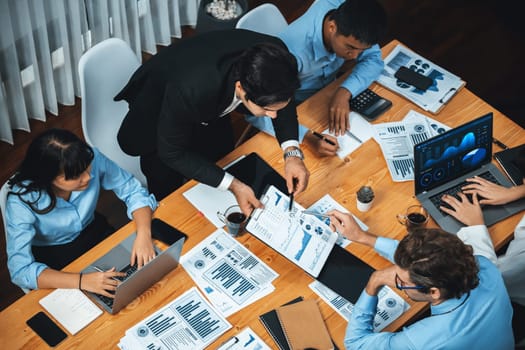 Wide top view of diverse group of business analyst team analyzing financial data report paper on meeting table. Chart and graph dashboard by business intelligence analysis. Meticulous