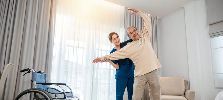 Rehabilitation of disabled people. Old senior man enjoys training with physiotherapist for outstretched arms at home, Asian physical therapist patient help elderly exercising arm stretch