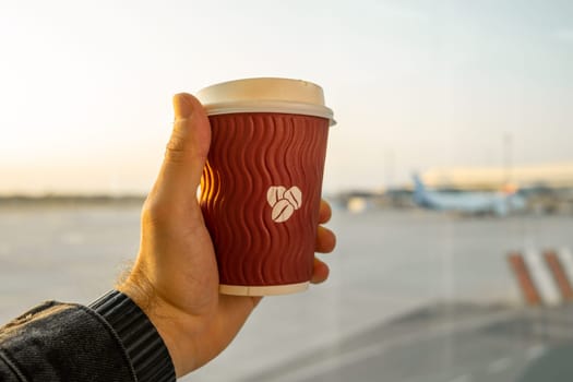 Cup of coffee in man hand with a aircraft on the background.