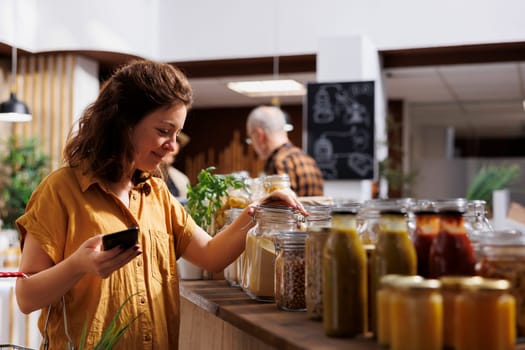 Green living woman on a diet using smartphone to make sure zero waste supermarket food is good for her health. Customer in local neighborhood eco friendly store making sure products are organic