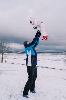 Dad throws up a little laughing girl while standing on a snowy hill. High quality photo