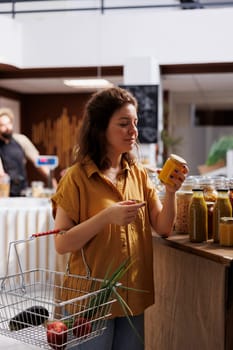 Green living woman in zero waste store interested in purchasing pesticides free produce with high nutritional value. Client does food shopping in environmentally friendly local neighborhood shop