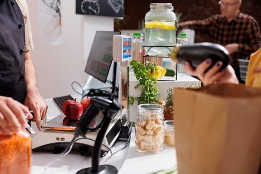 Close up of merchant at checkout counter in zero waste shop selling vegan products to environmentally conscious customers. Client buys healthy food with no additives in local neighborhood store