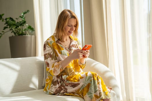 A young woman in a flowered dress using her mobile phone sitting in the hotel hall.