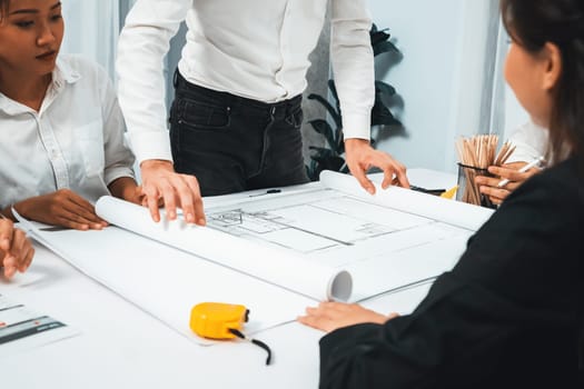 Diverse group of civil engineer and client working together on architectural project, reviewing construction plan and building blueprint at meeting table. Prudent