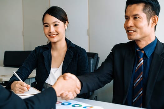 Business people agreement concept. Asian Businessman do handshake with another businessman in the office meeting room. Young Asian secretary lady sits beside him. uds