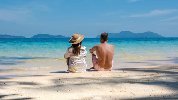a young couple of men and women sitting on a tropical beach during a luxury vacation in Thailand, diverse couple laying down on the beach of Koh Wai Island Thailand