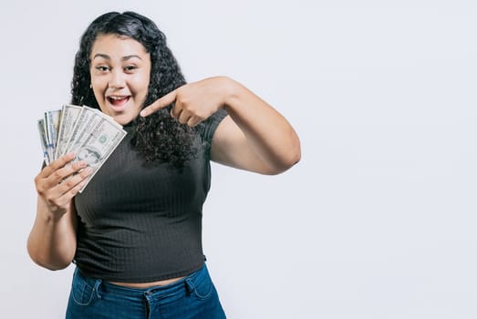 Smiling young woman holding and pointing money isolated. Attractive latin girl holding and pointing money. Latin people holding money