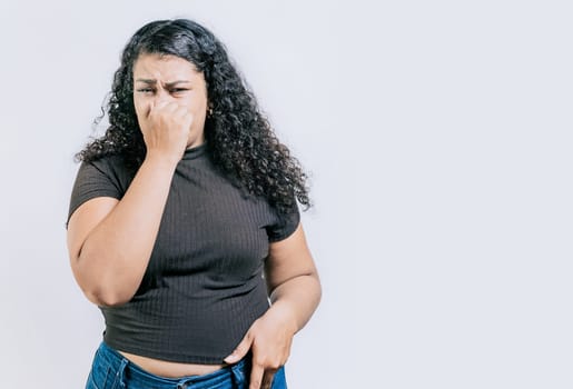 Latin woman covering nose from a bad smell isolated. Displeased girl holding her nose isolated. Disgust people covering nose