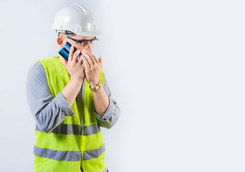 Male engineer talking on the phone secretly isolated. Young engineer in helmet talking on cell phone in silence, covering mouth