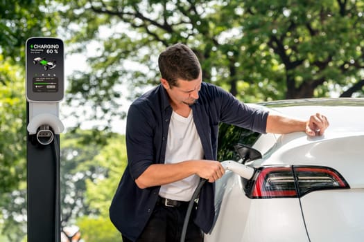 Man recharging battery for electric car during road trip travel EV car in natural forest or national park. Eco friendly travel during vacation and holiday. Exalt