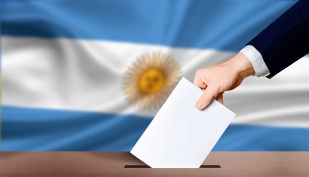 Argentina electoral elections concept. Hand holding ballot in voting ballot box with Argentina flag in background. Hand man puts ballot paper in voting box on Argentina flag background