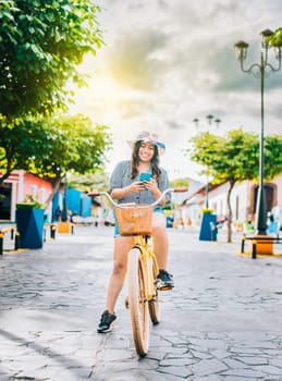 Happy tourist girl on bicycle using cell phone on the street. Beautiful girl in hat on bicycle with cell phone on the street of La Calzada, Granada, Nicaragua