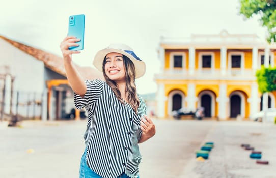 Happy tourist girl taking selfie in the cathedral of Granada. Young travel woman with hat taking a selfie in a square
