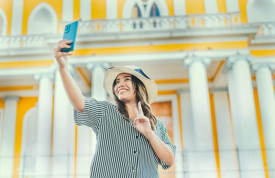 Young tourist woman with hat taking selfie in a square. Selfies and vacation concept. Beautiful tourist girl taking selfie in the cathedral of Granada
