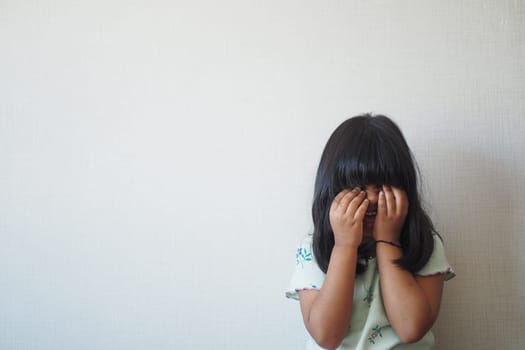 a upset child girl cover her face with hand .