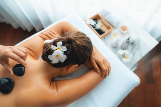 Hot stone massage at spa salon in luxury resort with day light serenity ambient, blissful woman customer enjoying spa basalt stone massage glide over body with soothing warmth. Quiescent