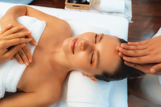 Caucasian woman enjoying relaxing anti-stress head massage and pampering facial beauty skin recreation leisure in dayspa modern light ambient at luxury resort or hotel spa salon. Quiescent