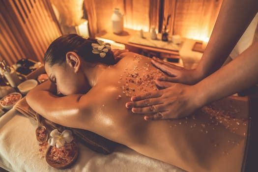 Woman customer having exfoliation treatment in luxury spa salon with warmth candle light ambient. Salt scrub beauty treatment in Health spa body scrub. Quiescent