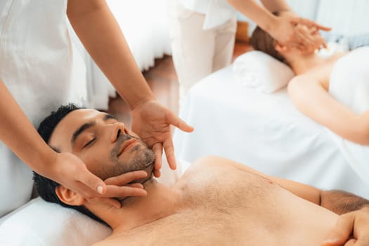 Caucasian couple enjoying relaxing anti-stress head massage and pampering facial beauty skin recreation leisure in dayspa modern light ambient at luxury resort or hotel spa salon. Quiescent