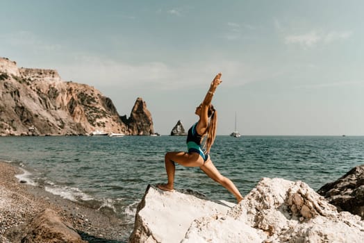 Yoga on the beach. A happy woman meditating in a yoga pose on the beach, surrounded by the ocean and rock mountains, promoting a healthy lifestyle outdoors in nature, and inspiring fitness concept