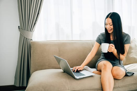 Relaxed woman on sofa enjoys remote education laptop coffee. Engaged in learning relaxation in cozy living room. Remote education and comfort. Joyful learning moments.