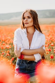 Happy woman in a poppy field in a white shirt and denim skirt with a wreath of poppies on her head posing and enjoying the poppy field