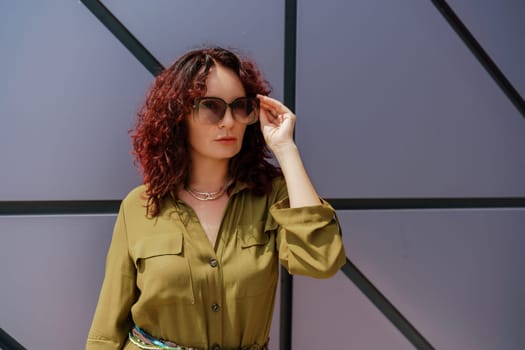 Portrait of a woman standing near a supermarket building. Caucasian model with long brunette hair, wears sunglasses and a khaki dress