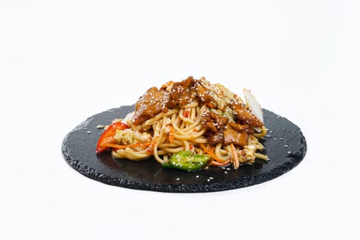 fried noodles with vegetables and meat in a flat plate on a white background