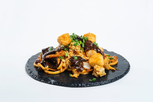 fried noodles with vegetables and meat in a flat plate on a white background