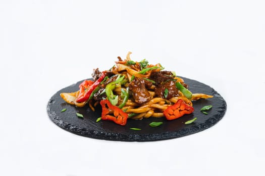 fried noodles with vegetables and meat in a flat plate on a white background