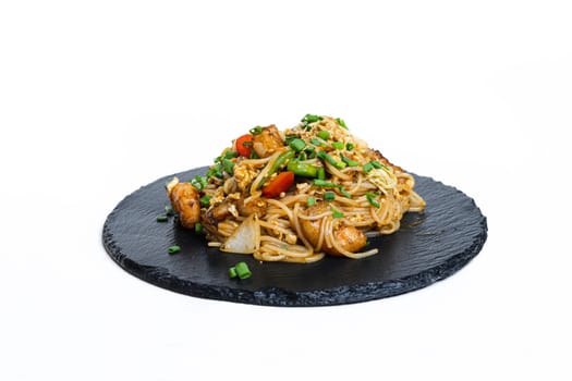 fried noodles with vegetables and meat in a flat plate on a white background