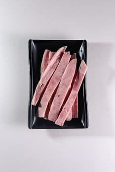 sliced boiled meat on a black plate on a white background