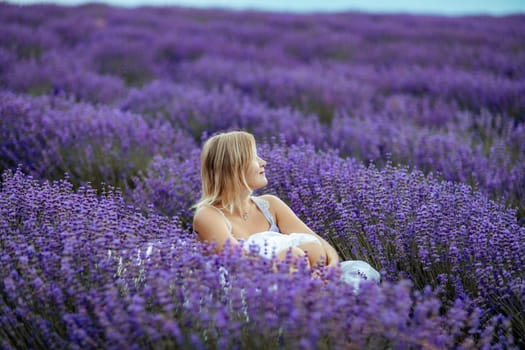 A middle-aged woman sits in a lavender field and enjoys aromatherapy. Aromatherapy concept, lavender oil, photo session in lavender.