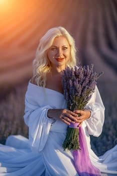 Blonde woman poses in lavender field at sunset. Happy woman in white dress holds lavender bouquet. Aromatherapy concept, lavender oil, photo session in lavender.