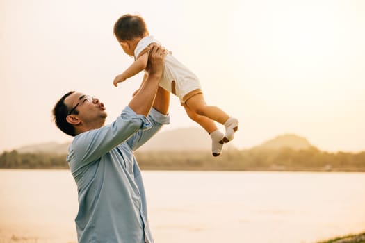 A happy dad and his toddler son share a playful moment of freedom and joy in the park, throwing him up in the air on a sunny summer day. Family love and happiness captured in a photograph