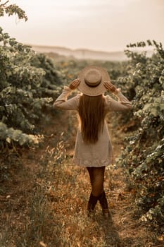 Woman with straw hat stands in front of vineyard. She is wearing a light dress and posing for a photo. Travel concept to different countries.