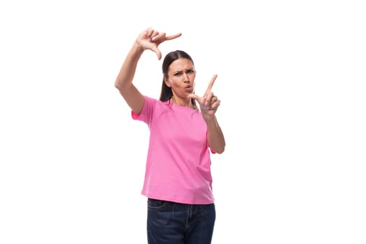 young positive good-looking woman with black hair dressed in a pink t-shirt makes a frame from her hands.