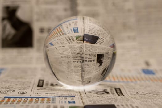 A glass globe reveals the letters inside, with a newspaper in the background.