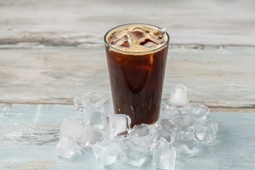 A cup of Iced Americano Coffee with ice cubes placed on a wooden table in a coffee shop. Top view of a glass of coffee.