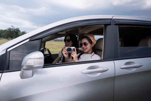 Young happy Asian girl friends laughing and smiling in car during a road trip to vacation.