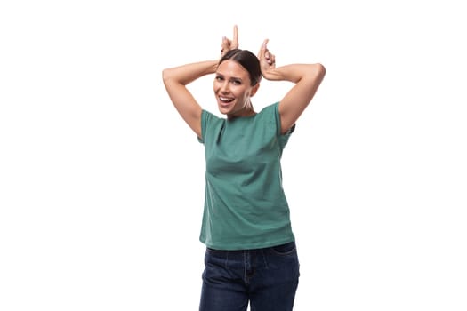 30 year old positive european brunette woman with a ponytail hairstyle is dressed in a green t-shirt and jeans on a white background with copy space.