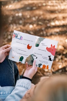 Book with colorful pictures in women hands in the park. Cropped. Faceless. High quality photo
