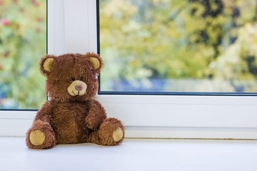 Brown bear toy sits on a windowsill close up, copy space
