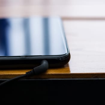 Black smartphone with headphones on a wooden table, square photo format