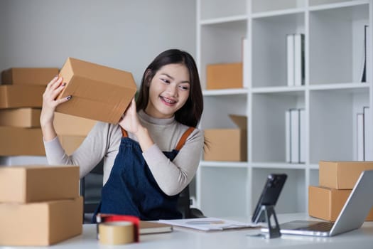 Startup SME small business entrepreneur SME or freelance Asian woman using a laptop with box, online marketing packaging box and delivery, SME concept..